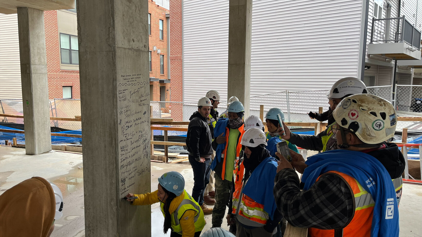 A group of people sign a pillar within a construction site, marking the construction team reaching the top of the structure.