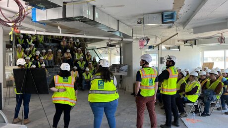 Construction professionals stand in front of a crowd of students. Every person has a safety vest and hard hat.