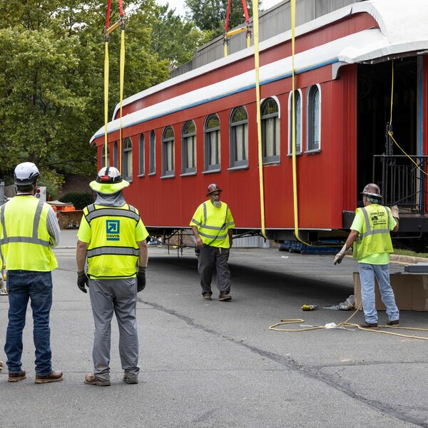 A group of construction workers stands near a red railcar
