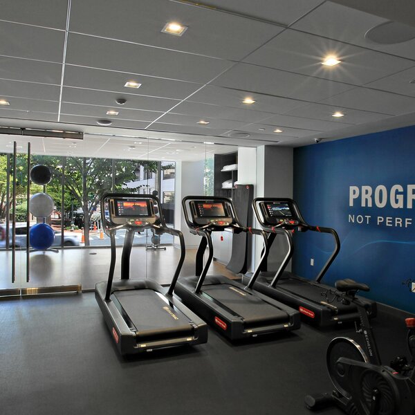 A renovated fitness center that includes three treadmills and a wall decal that reads "Progress, not Perfection"