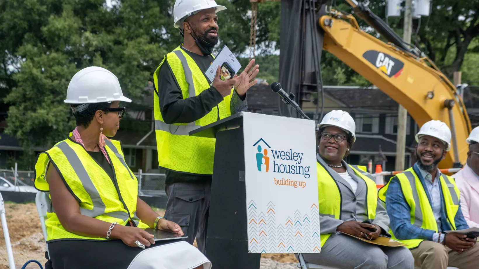 People with construction gear sit at a panel for a groundbreaking ceremony.