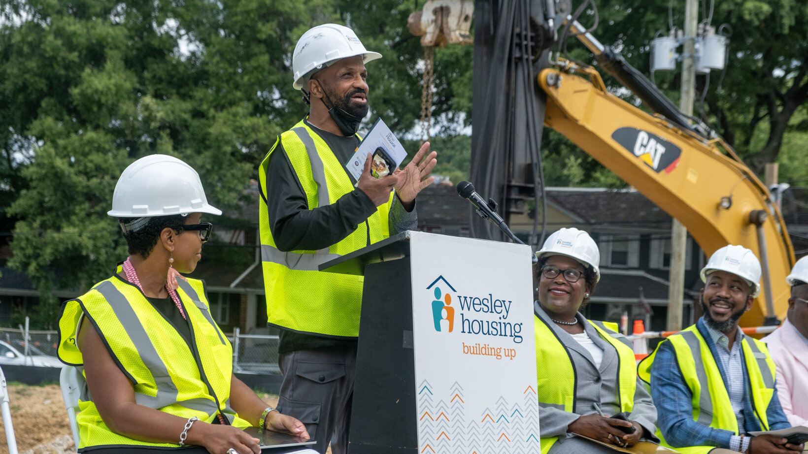 People with construction gear sit at a panel for a groundbreaking ceremony.