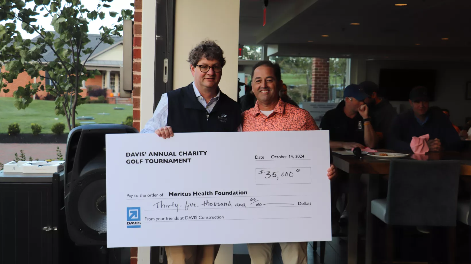 Two men stand together holding a large check, made out to Meritus Health for 35,000 dollars.