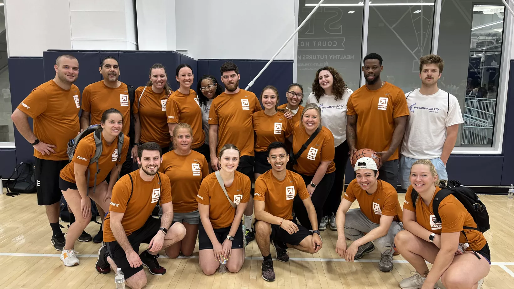 Group photo of a team in a gymnasium wearing matching orange shirts