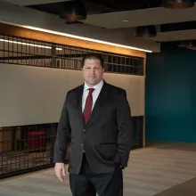 A man in professional wear stands in a hallway.