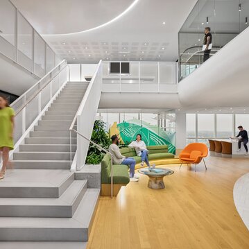 Shot of an office space with a large staircase connecting two floors, and employees walking around.