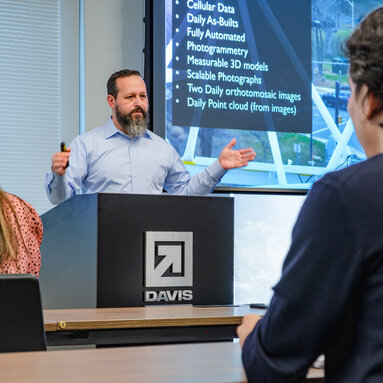 A man in professional wear stands at a podium giving a lecture.