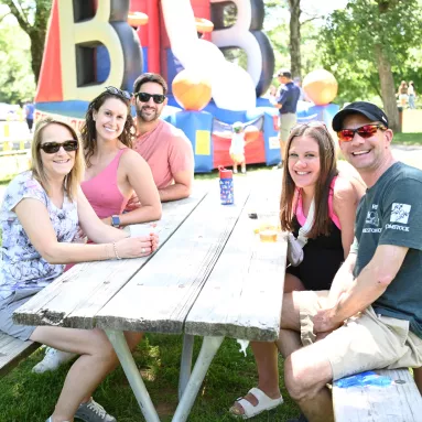 Five adults sit at a picnic table and smile for the camera.