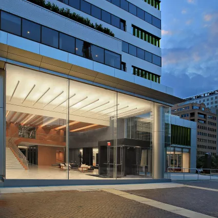 Exterior shot of a renovated building at night. The lobby of the building is lit up.