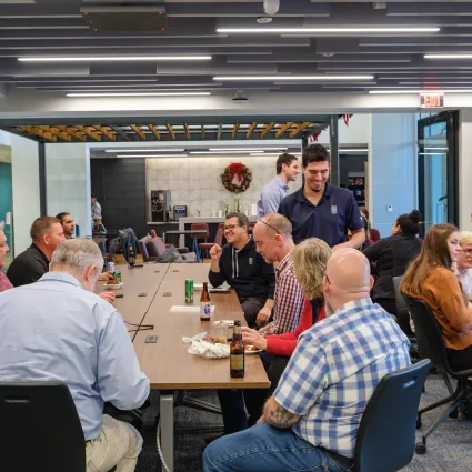 A group of employees gather and talk at tables in a large room.