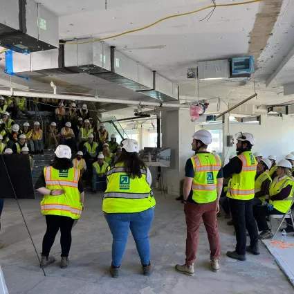 Construction professionals stand in front of a crowd of students. Every person has a safety vest and hard hat.