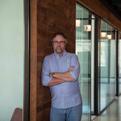 A man in professional wear stands in a hallway.