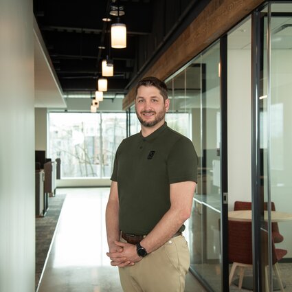 A man in professional wear stands in a hallway.