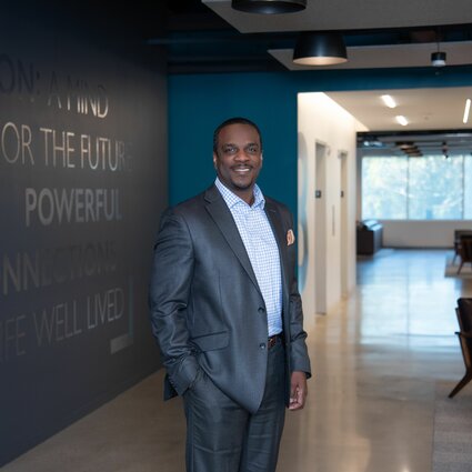 A man in professional wear stands in a hallway.