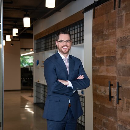 A man in professional wear stands in a hallway.