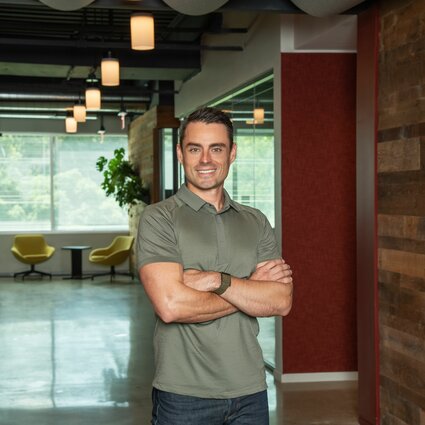 A man in professional wear stands in a hallway.