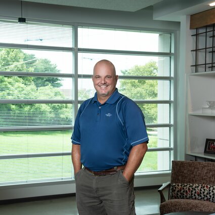 A man in professional wear stands in a hallway.