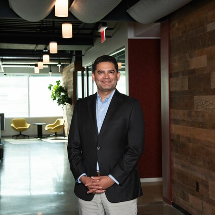 A man in professional wear stands in a hallway.