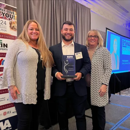 A man standing in between two women and holding an award