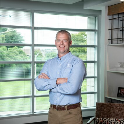 A man in professional wear stands in a hallway.