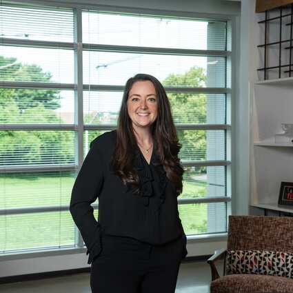 A woman in professional wear stands in a room.