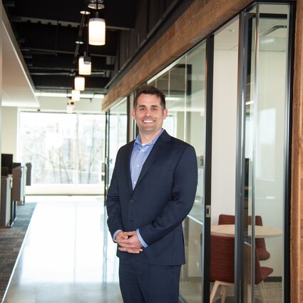 A man in professional wear stands in a hallway.