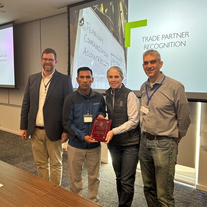 Four people pose for a photo--one man is being presented with an award by two other men and one woman.