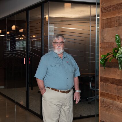 A man in professional wear stands in a hallway.