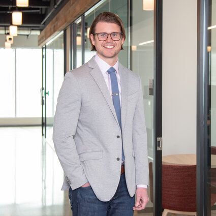 A man in professional wear stands in a hallway.