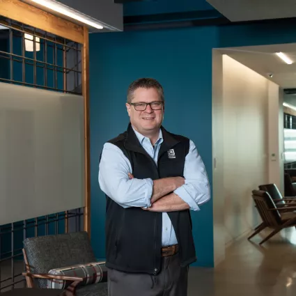 A man in professional wear stands in a hallway.