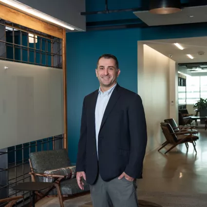 A man in professional wear stands in a hallway.