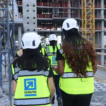 Two women walk on a construction site in the foreground. Others are in the background