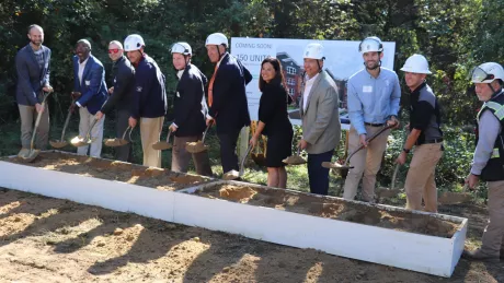 eleven people with hard hats and shovels poised to dig into dirt.