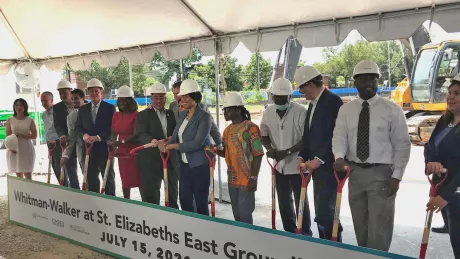 LIne of people wearing hardhats with shovels poised to dig into dirt.