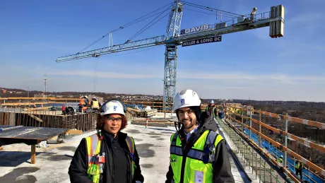 a woman and man wearing hard hats standing in front of a crane