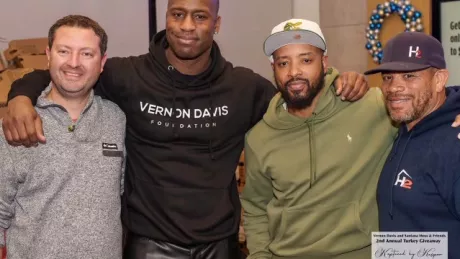 Four men (two of them football players) stand and pose for a picture at a Thanksgiving turkey giveaway event.