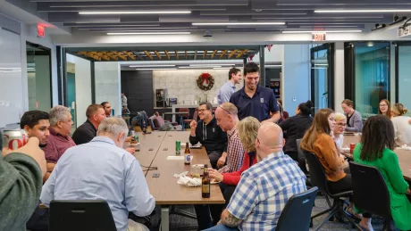 A group of employees gather and talk at tables in a large room.