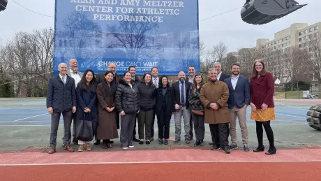 A group of people stand together in front of a sign commemorating the groundbreaking of the Meltzer Center, a new Sports Facility at American University.