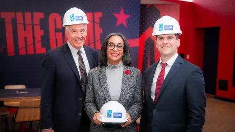 Two men and a woman stand together at a gala in construction helmets and formal attire