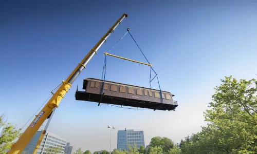 A crane lifts a brown railcar high in the air