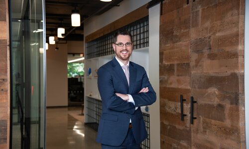 A man in professional wear stands in a hallway.