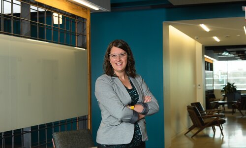 A woman in professional wear stands in a hallway.