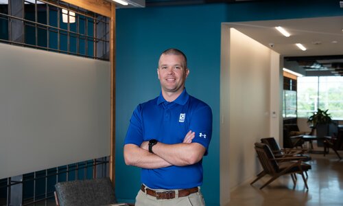 A man in professional wear stands in a hallway.