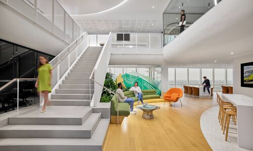 Shot of an office space with a large staircase connecting two floors, and employees walking around.