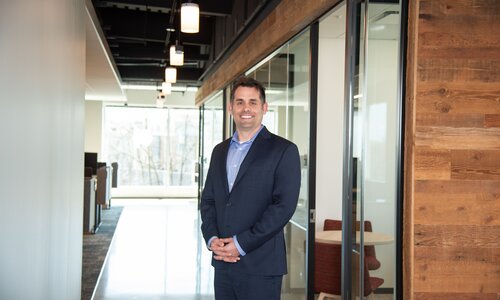 A man in professional wear stands in a hallway.