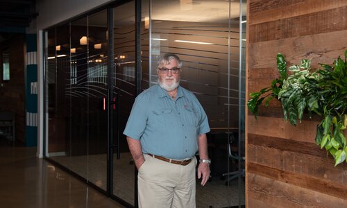 A man in professional wear stands in a hallway.