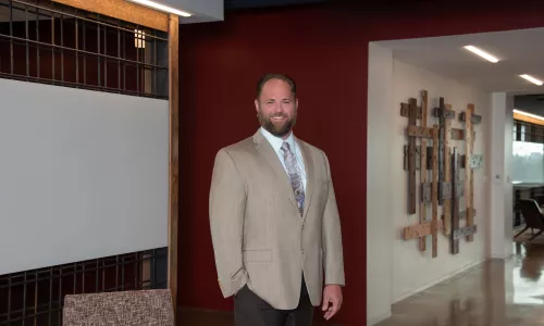 A man in professional wear stands in a hallway.