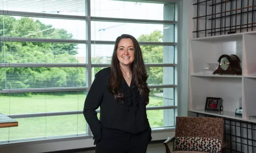 A woman in professional wear stands in a hallway.