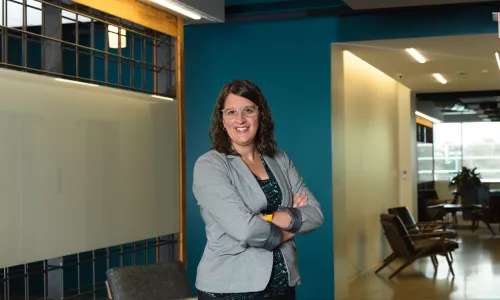 A woman in professional wear stands in a hallway.