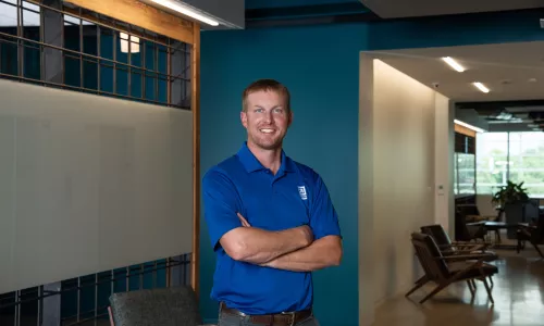 A man in professional wear stands in a hallway.